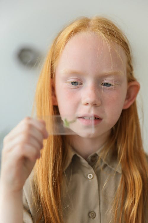 A young student holding a glass slide with a green bacterial sample in it.